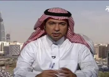 A man wearing a white thobe and red-and-white checkered ghutra sits in front of a cityscape with modern buildings. The logo of Al Arabiya is visible in the top right corner.